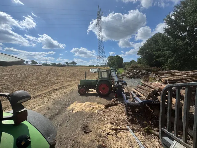 Traktor mit Spaltanlage und Rundholzpolter auf dem Feld